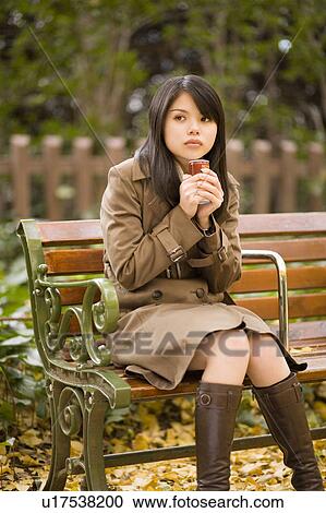 Stock Image - Young woman sitting on bench. Fotosearch