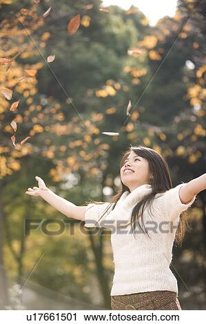 Stock Image - Young woman throwing fallen leaves. Fotosearch