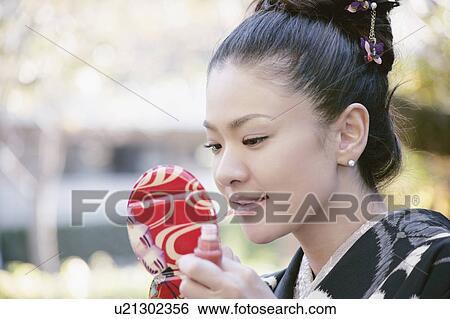 Stock Photograph - Young woman in kimono applying make-up. Fotosearch