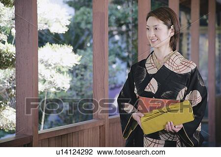 Stock Image - Young woman in kimono holding gift box. Fotosearch