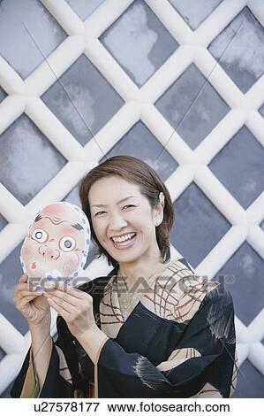 Stock Photo - Young woman in kimono holding mask up to face. Fotosearch