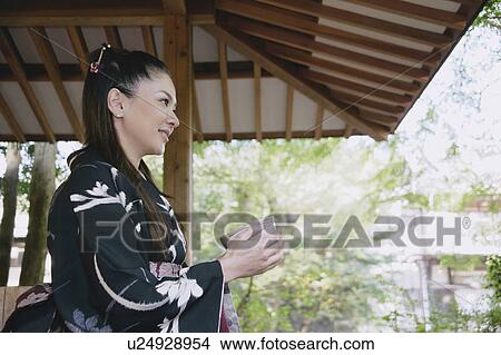 Picture - Young woman in kimono holding tea cup. Fotosearch