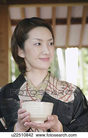 Stock Image - Young woman in kimono holding tea cup. Fotosearch
