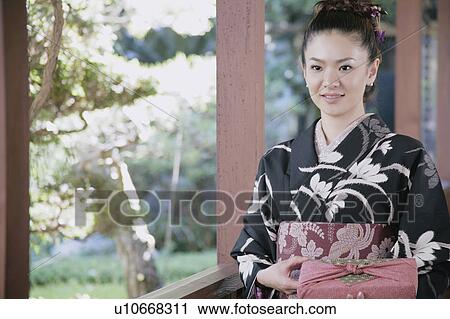 Stock Image - Young woman in kimono holding wrapped gift. Fotosearch