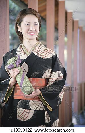 Stock Image - Young woman in kimono holding wrapped gift. Fotosearch