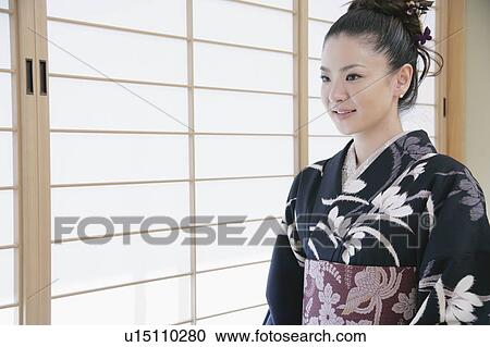 Stock Image - Young woman in kimono sitting on floor. Fotosearch