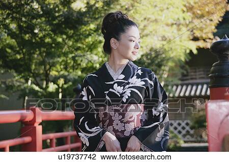 Stock Image - Young woman in kimono standing on bridge. Fotosearch