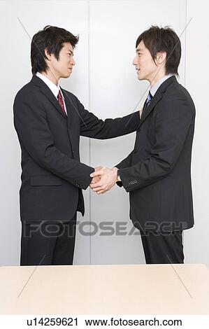 Stock Image - Two young businessmen shaking hands. Fotosearch
