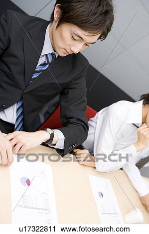 Young businessman checking watch during meeting View Large Photo Image Stock Image - Young businessman checking watch during meeting. Fotosearch