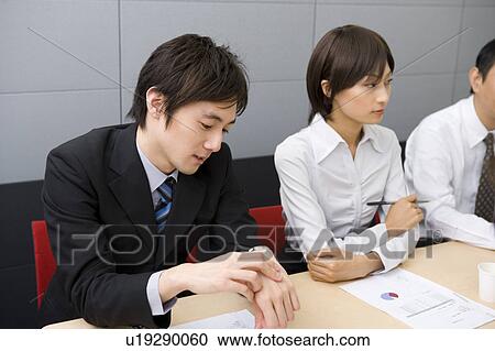Stock Image - Young businessman checking watch during meeting. Fotosearch