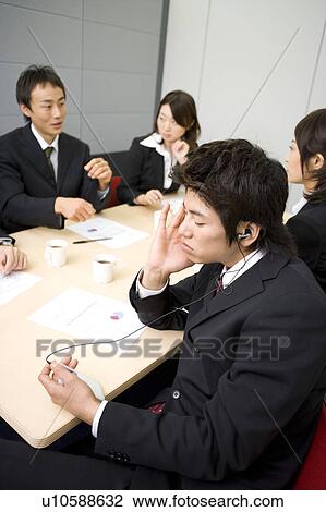 Stock Image - Young businessman listening to music during meeting. Fotosearch