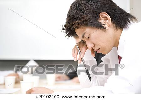 Stock Image - Young businessman sleeping during meeting. Fotosearch