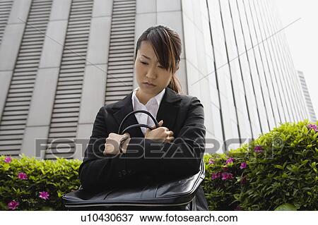 Stock Photo - Young woman looking down holding bag. Fotosearch