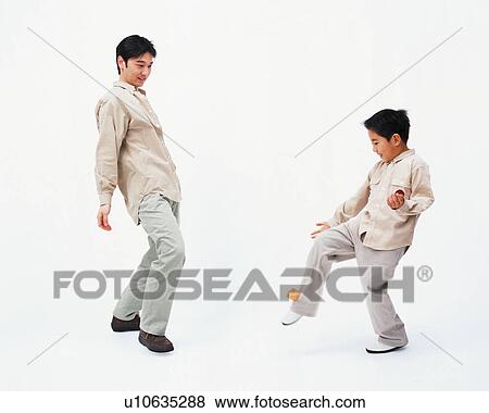 Stock Photo - A boy trying to catch a small cube with his leg while father watches. Fotosearch