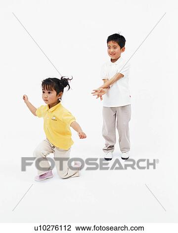 Stock Image - A small boy smiling while his younger sister bends down on knee. Fotosearch