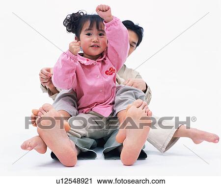 Stock Image - Front view of a cute girl sitting on her father's lap showing a punching action. Fotosearch