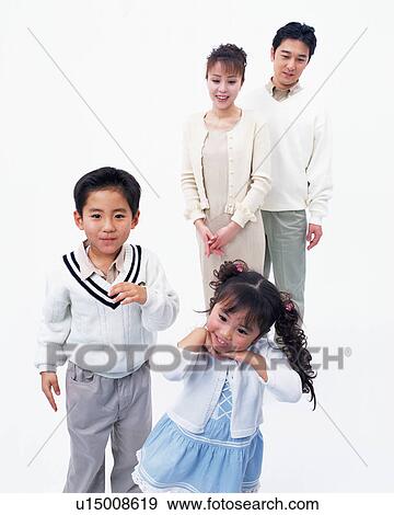 Stock Photo - Two children posing in front of camera with their parents in the background. Fotosearch
