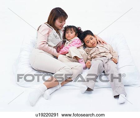 Stock Image - Two children resting on couch along with their mother. Fotosearch