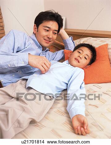 Picture - A boy lying on bed with his father. Fotosearch