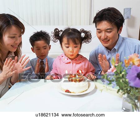 Picture - A girl blowing out candles on cake and celebrating her birthday with her family. Fotosearch