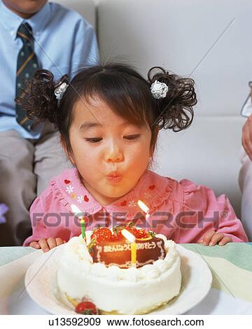 Stock Photo - A girl blowing out candles on her birthday cake. Fotosearch