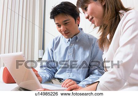 Stock Photograph - A man along with his wife looking at laptop. Fotosearch