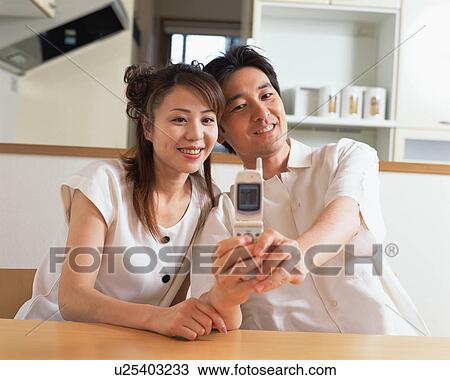 Stock Image - A man capturing an affectionate moment with his wife on mobile phone. Fotosearch