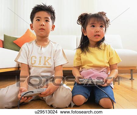 Picture - A small boy playing video game along with his sister. Fotosearch