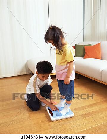 Picture - A small girl standing on scale while her brother presses button. Fotosearch