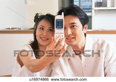 Stock Photograph - A woman capturing an affectionate moment with her husband on mobile phone. Fotosearch
