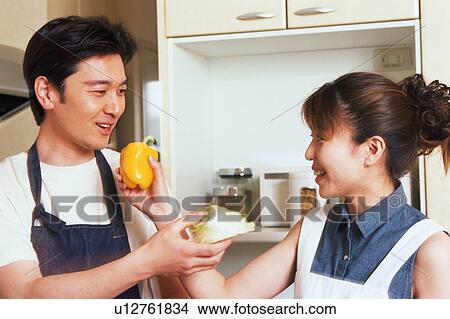 Picture - A woman giving a bell pepper to her husband while the husband gives her lettuce. Fotosearch