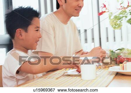 Stock Photo - Side view of a boy smiling while having his meal. Fotosearch