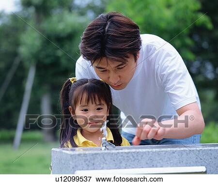 Stock Photo - A girl looking at tap water with her father. Fotosearch
