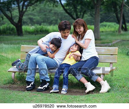 Stock Image - Family sitting on a bench in a park. Fotosearch
