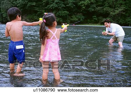 Stock Image - Father and children playing with squirt guns. Fotosearch