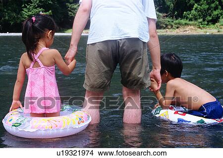 Picture - Father holding hands of children in a river. Fotosearch