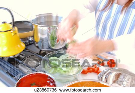 Stock Photograph - A young woman cooking in a kitchen. Fotosearch