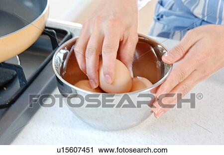 Stock Image - A young woman trying to crack an egg. Fotosearch