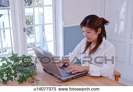 Stock Image - A young woman using computer at home. Fotosearch