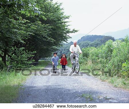 Stock Photo - A grand father riding a bicycle with grand children walking. Fotosearch