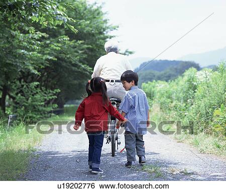 Stock Photograph - A senior man riding a bicycle with grand children walking after. Fotosearch