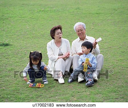 Stock Image - Senior couple playing with grand children in a park. Fotosearch