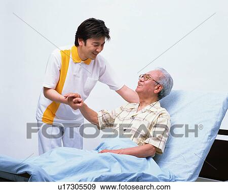 Stock Photo - A senior man in a bed talking with caretaker. Fotosearch