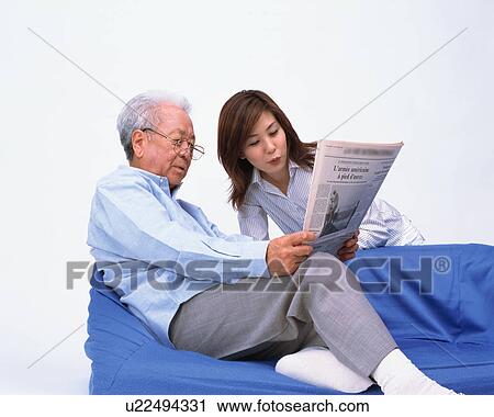 Stock Image - A senior man reading newspaper with his daughter. Fotosearch