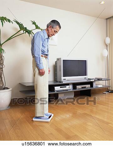 Stock Image - A senior man weighing in a living room. Fotosearch