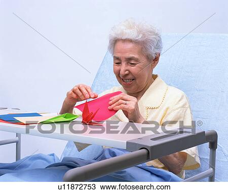 Stock Image - A senior woman in a bed playing with origami. Fotosearch