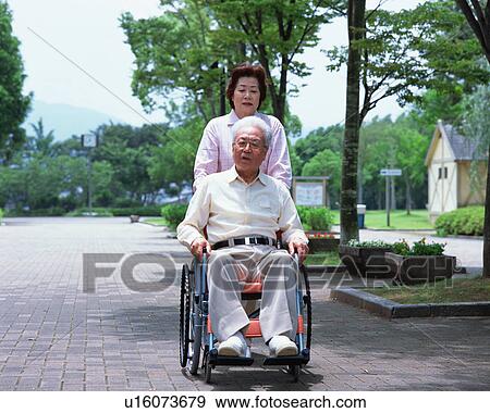 Stock Photo - A senior woman pushing a senior man in a wheel chair. Fotosearch