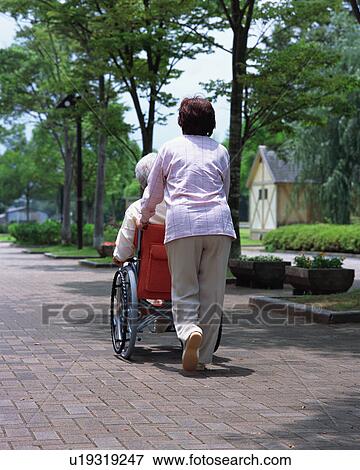 Stock Photo - A senior woman pushing a senior man in a wheel chair. Fotosearch