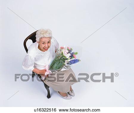 Stock Photograph - A senior woman sitting in a chair with flower bouquet. Fotosearch