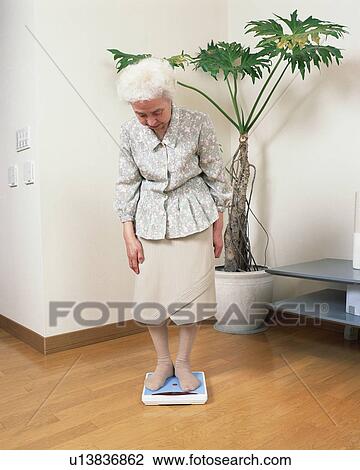 Stock Image - A senior woman weighing in a living room. Fotosearch